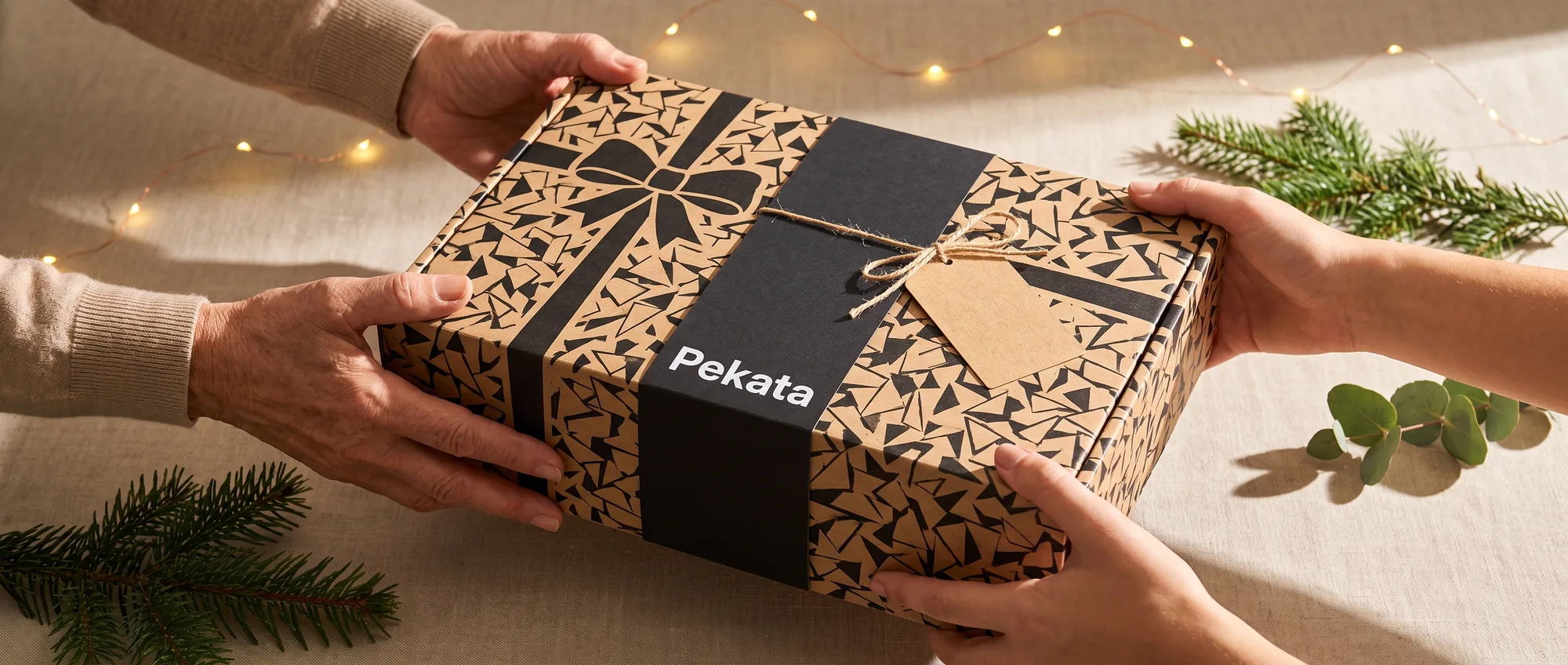 Due paia di mani che consegnano e ricevono una scatola regalo Pekata con etichetta kraft e stampa trencadís